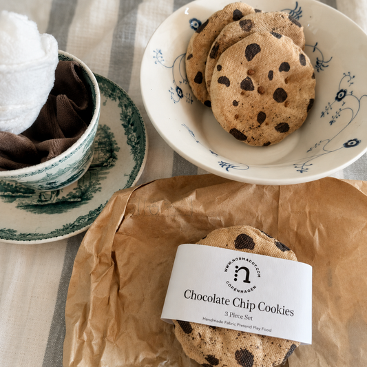 Handmade fabric chocolate chip cookies with paper band, styled with a vintage teacup, ceramic bowl and brown paper.