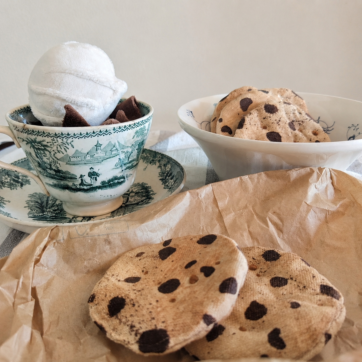 Handmade fabric chocolate chip cookies in a cozy tea setting with vintage cup, ceramic bowl and brown paper.