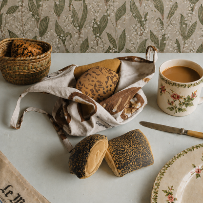 Pretend Baked goods in a basket with a cup of coffee on a table with floral-patterned wallpaper.