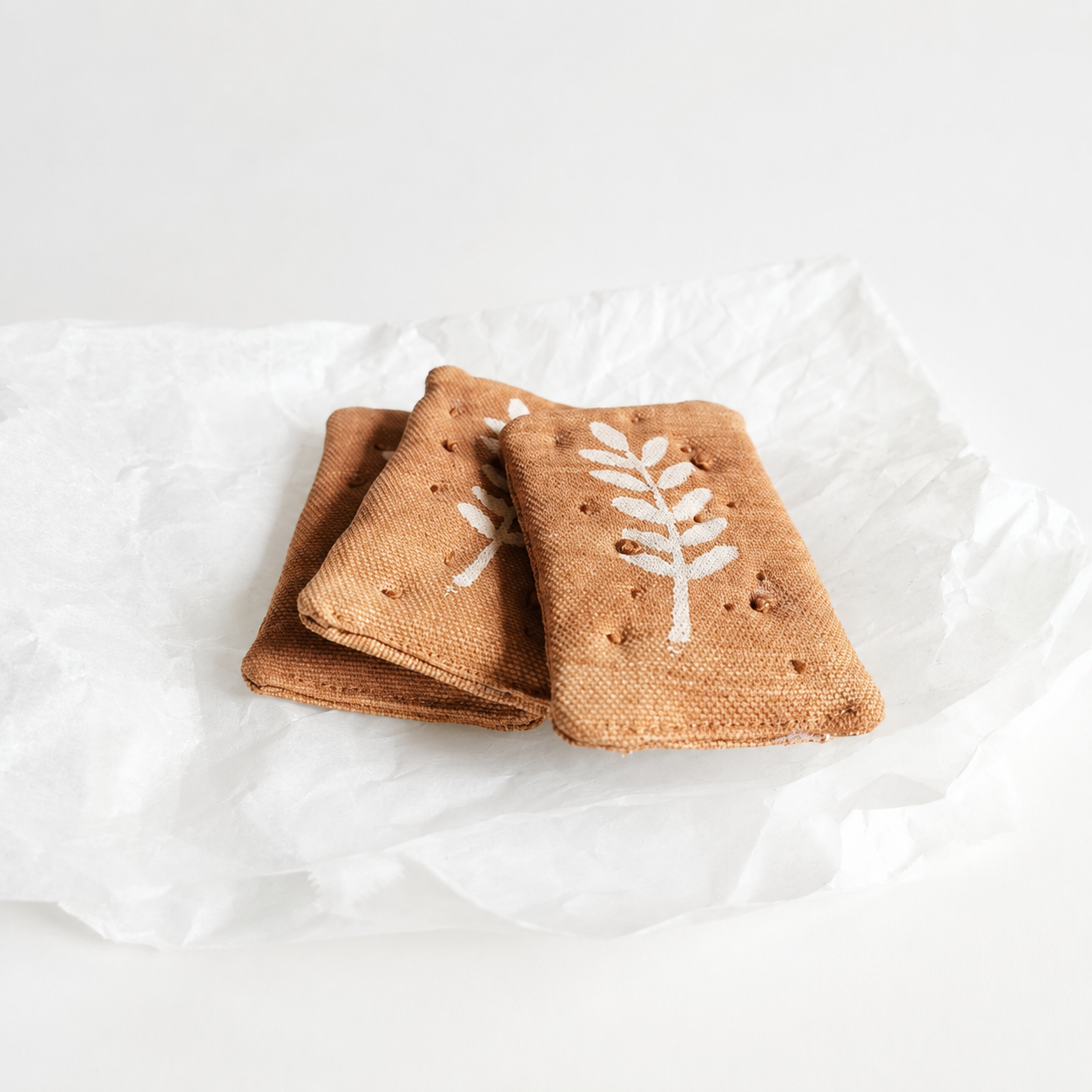 Handmade fabric crispbread crackers with printed grain details, photographed on white paper for a clean studio product image.