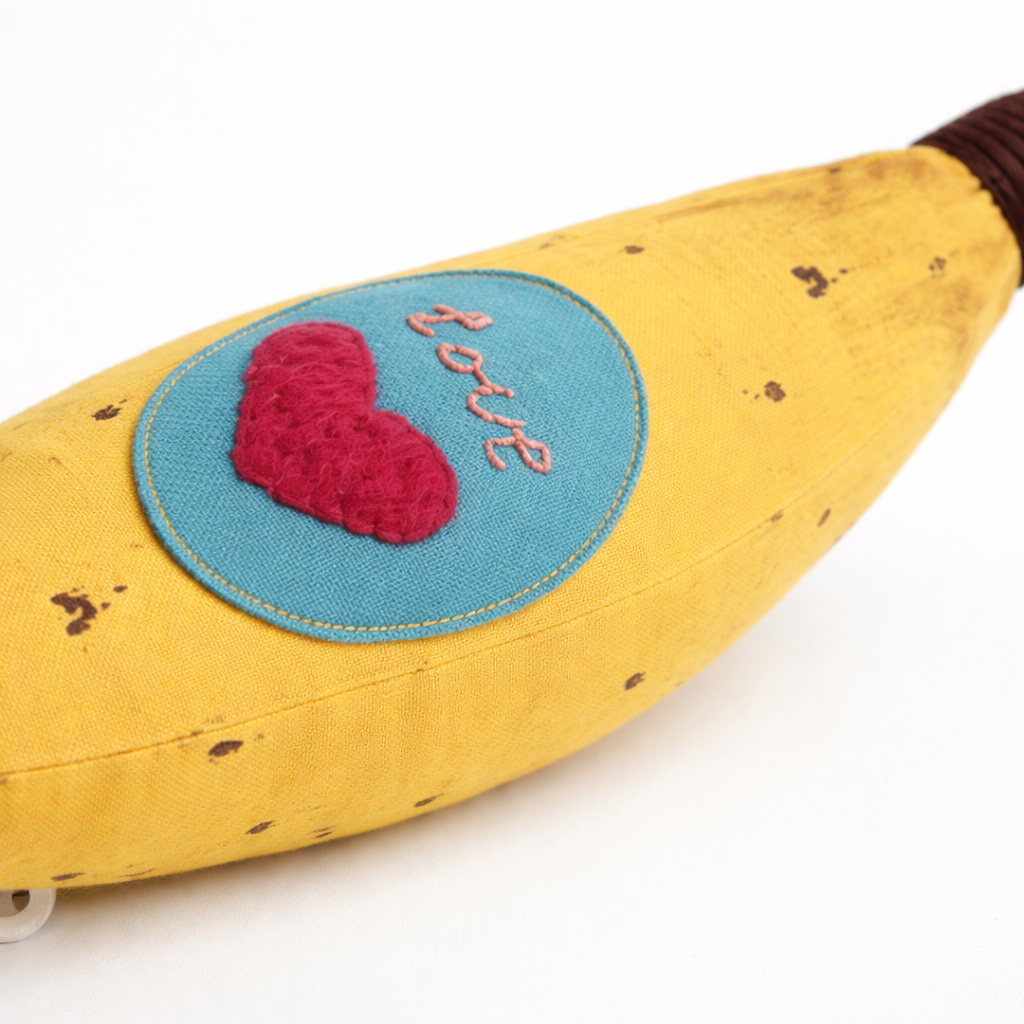 Banana-shaped pillow with a heart and 'love' patch on a white background