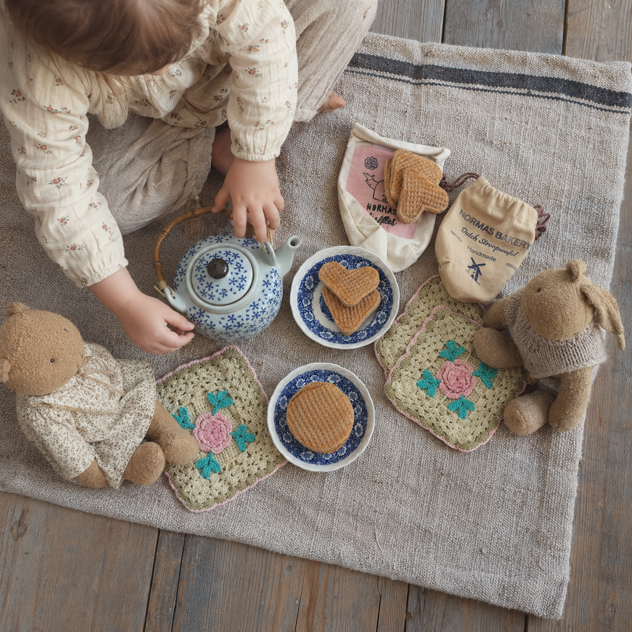 Child playing tea party with handmade Dutch stroopwafel toys, vintage teapot and teddy bears