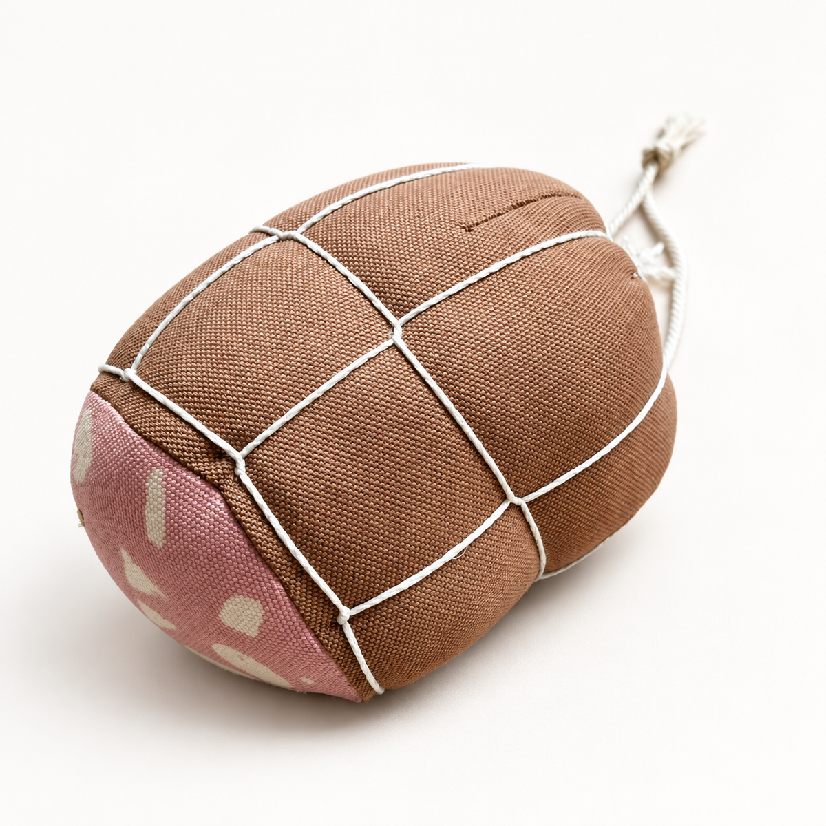 Handmade fabric mortadella play food in brown cotton canvas with white string netting and a pink patterned end, photographed on a soft off-white studio background.