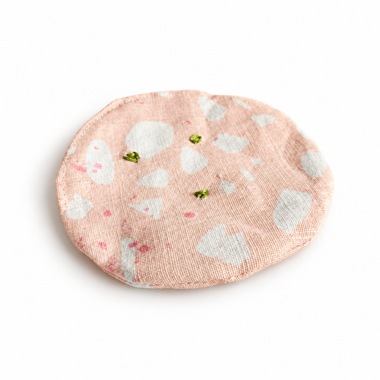 Handmade upcycled fabric mortadella slice in soft pink with white marbling and hand-embroidered green pistachios. Textile play food by normadot, made in Denmark.