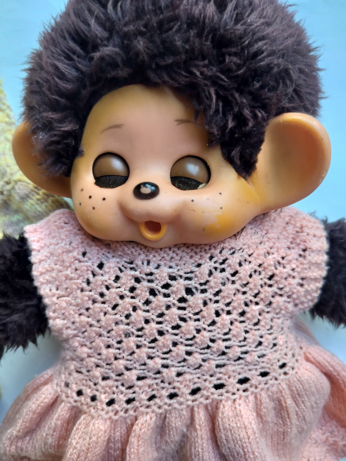 Close-up of a vintage Monchhichi doll with dark plush fur, painted face and handmade pink knitted dress
