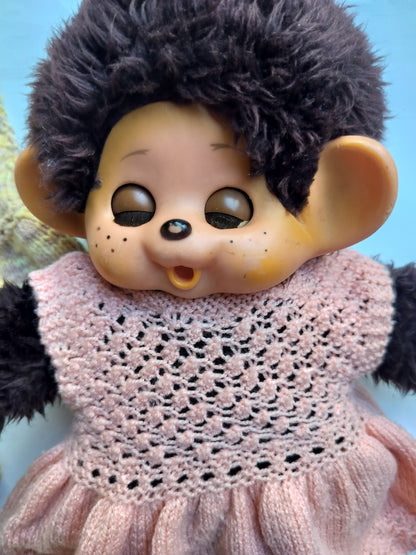 Close-up of a vintage Monchhichi doll with dark plush fur, painted face and handmade pink knitted dress