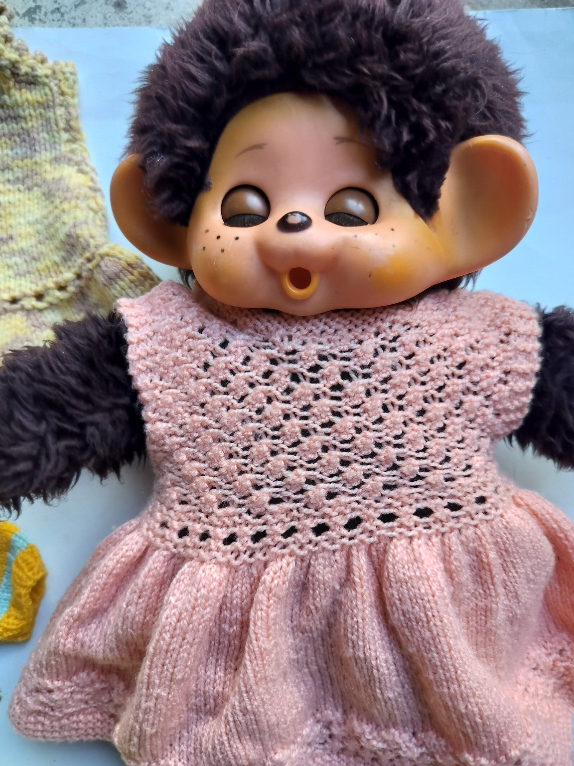 Close-up of a vintage Monchhichi doll wearing a handmade pink knitted dress.