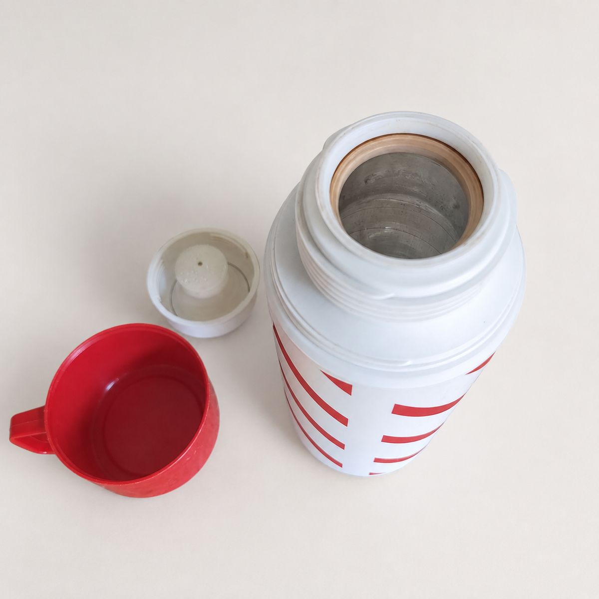 Open vintage red and white striped thermos flask shown with its red cup and white stopper, revealing the metal interior.