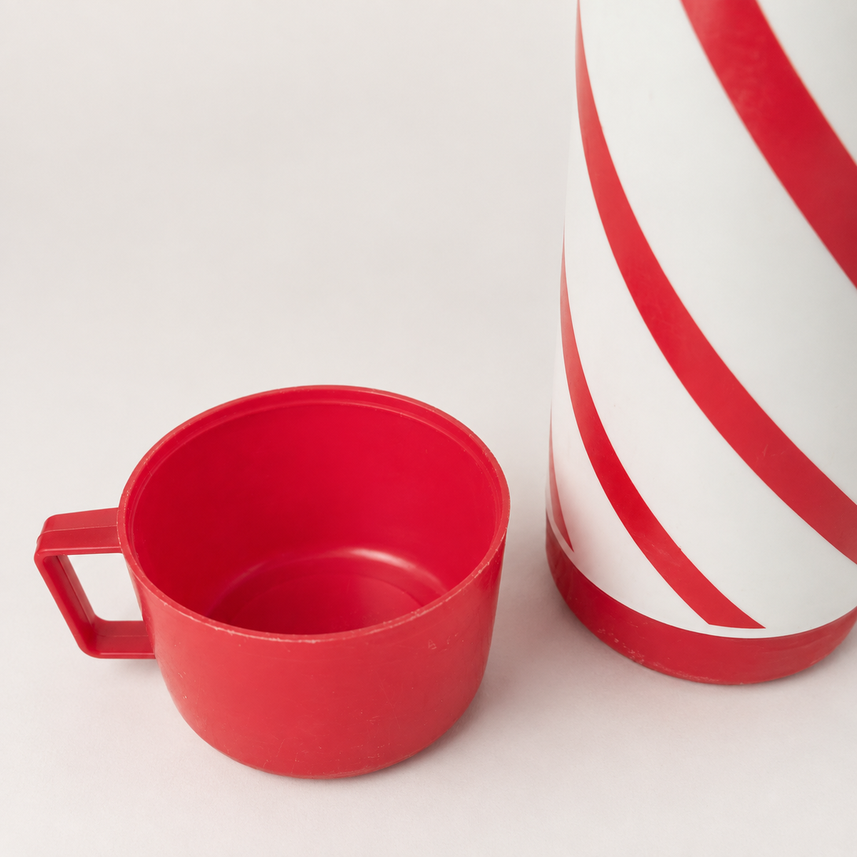 Vintage red and white striped thermos flask with matching red drinking cup, shown in close-up.