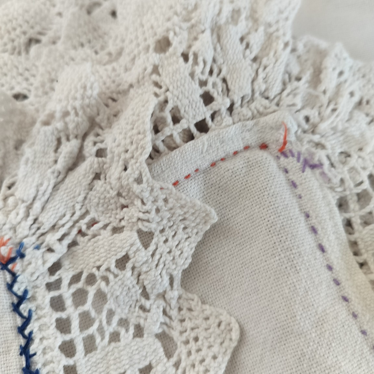 Close-up of the off-white tablecloth’s crocheted lace corner with blue, orange and purple stitching
