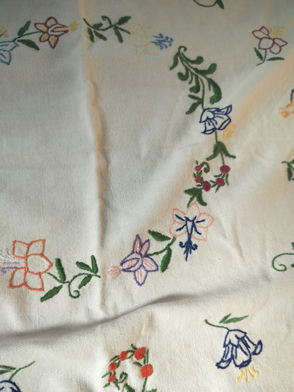 Close-up of colourful embroidered flowers and green leaves on the off-white vintage tablecloth