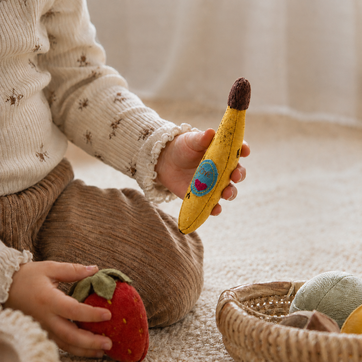 Child playing with a handmade fabric banana toy and soft fruit toys on a cozy neutral rug.
