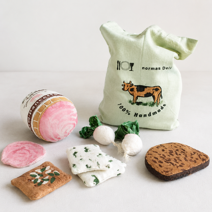 Handmade fabric deli play food set with Pancetta, radishes, crackers, cheese pieces, bread slice and Normas Deli tote bag in a light studio setting.