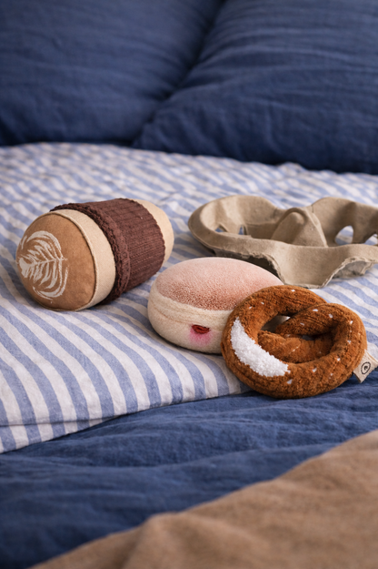 Handmade Berliner Pfannkuchen play food toy displayed with a soft pretzel and fabric bakery items on blue striped bedding