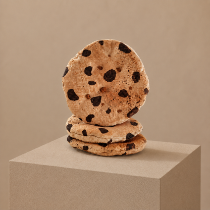 Handmade fabric chocolate chip cookies displayed as an art object on a neutral museum-style pedestal.