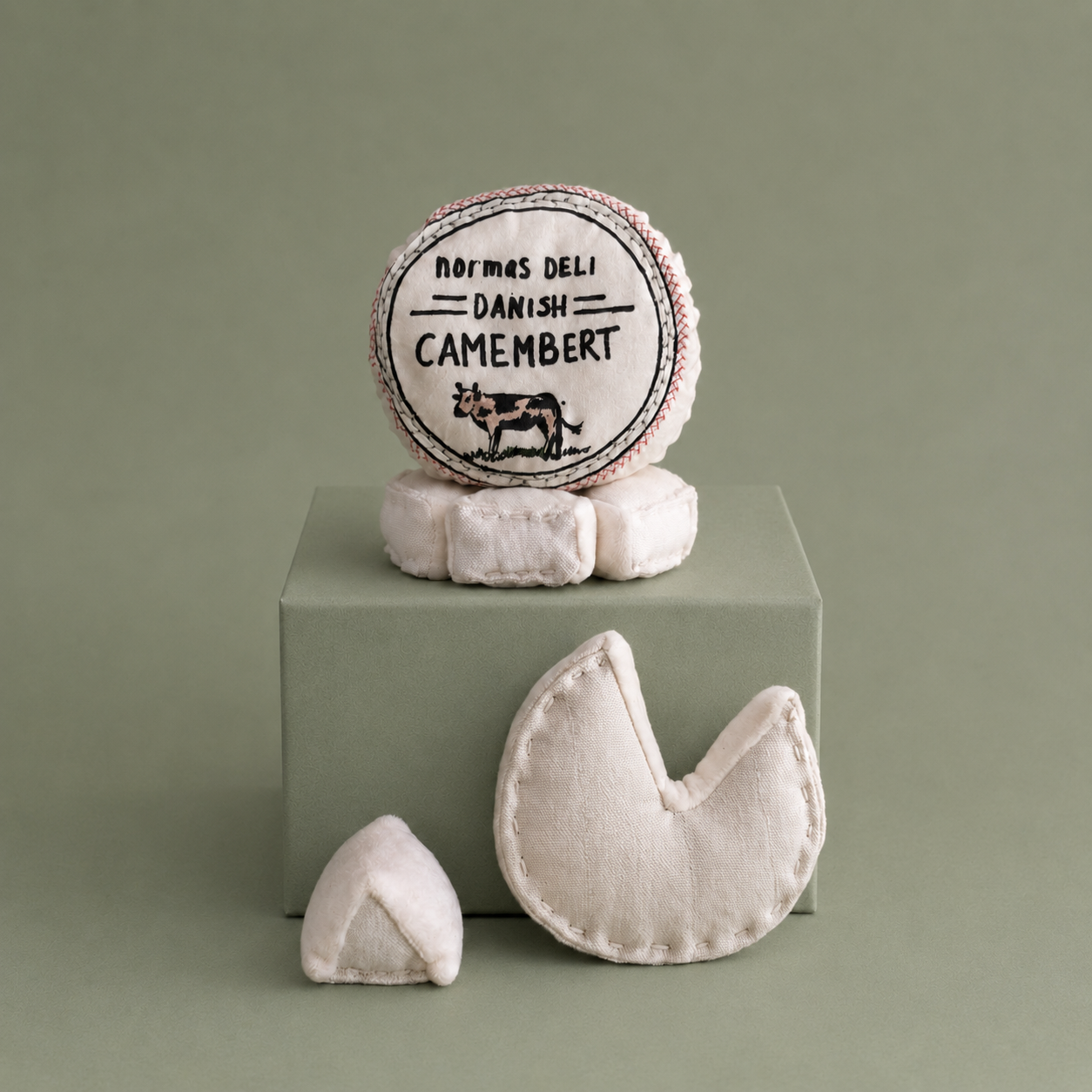 Handmade textile camembert cheese play food with removable printed cover, soft round cheese and small cheese wedge on brown paper for pretend play kitchens