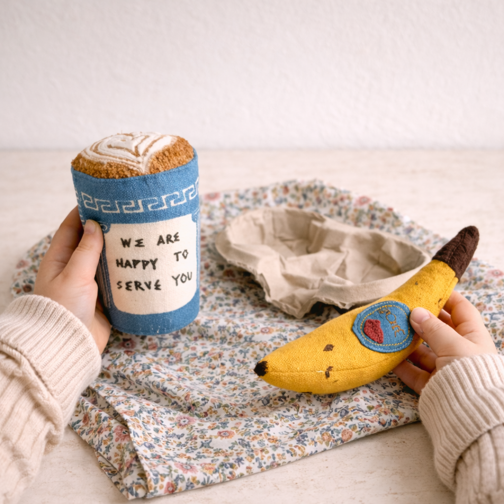 Person holding a toy cup and banana with a patch on a floral blanket